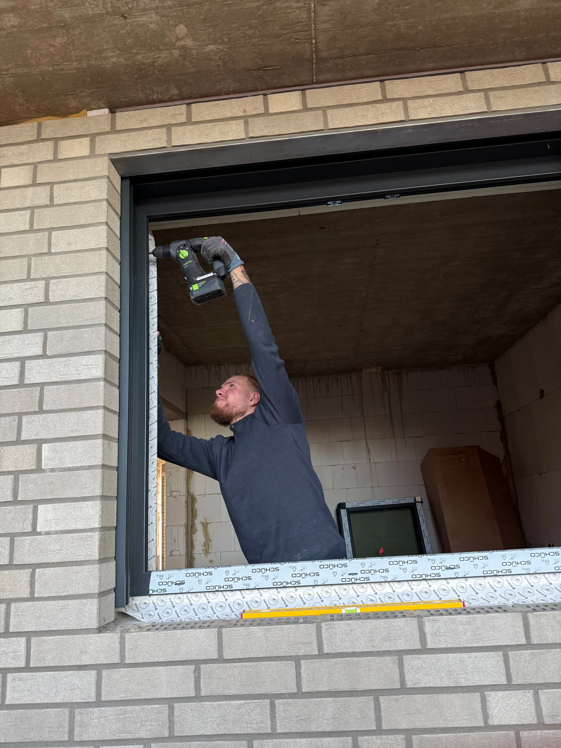 Leonardo bohrt Befestigungslöcher für einen Fensterrahmen mit dem Festool BHC 18 auf der Baustelle